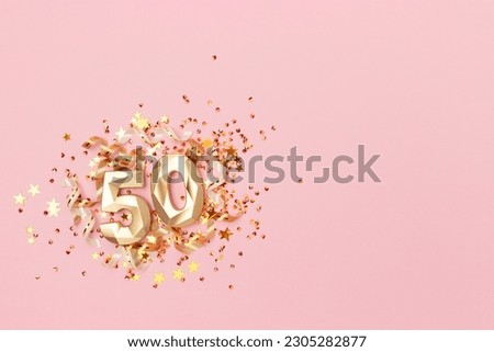 Golden number fifty, ribbons and stars confetti on a pink background. Festive creative concept with copy space.