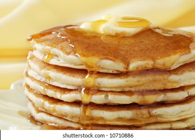 Golden pancakes with butter and warm maple syrup.  Close-up with extremely shallow dof and soft yellow background.