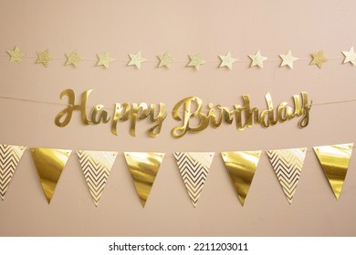 Golden party  inscription happy birthday, garland flags and stars. Beige festive background with copy space. - Shutterstock ID 2211203011