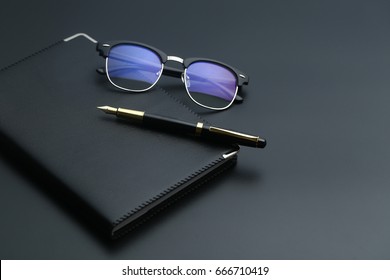 golden pen,notebook,calculator and glasses on black desk