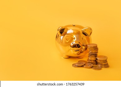 Golden Piggy Bank With Money Towers On Yellow Background. Stack Of Euro Coins Near Golden Money Box. Money Pig, Money Saving, Moneybox, Finance And Investments Concept. Free Space For Text