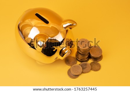 Golden piggy bank with money towers on yellow background. Stack of euro coins near golden money box. Money pig, money saving, moneybox, finance and investments concept. Free space for text