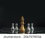 Golden queen chess piece standing in the center of little silver pawn pieces on chessboard on dark background. Games of chess figure in chess game competition. Leadership, business strategy concept.