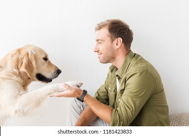 golden retriever dog giving paw to happy man against white wall - Shutterstock ID 1181423833