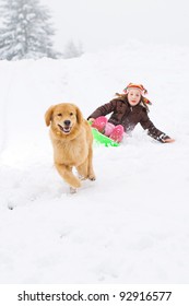 A Golden Retriever Dog Pulling A Child On A Sled Down A Snow Covered Hill.