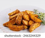 Golden roasted potato wedges seasoned with spices, garnished with herbs on a white background