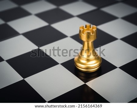 The golden rook chess piece standing alone on chess board background. Rook or the castle, the tower symbolize a protectorate of the city.