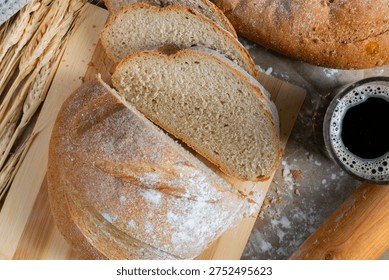 Golden rustic bread loaf partially sliced on wooden surface, paired with a glass of kvass and wheat stalks for a wholesome traditional scene