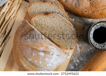 Golden rustic bread loaf partially sliced on wooden surface, paired with a glass of kvass and wheat stalks for a wholesome traditional scene