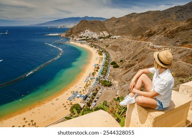 Golden sands and blue waters of Las Teresitas beach seen from above, with a woman in a straw hat taking in the coastal view of Tenerife - Powered by Shutterstock