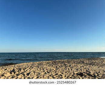 Golden sandy beach with calm blue waters under a clear sky. Gentle waves lap the shore, creating a serene and inviting coastal scene. Perfect for themes of relaxation, travel, and natural beauty. - Powered by Shutterstock