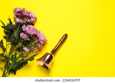 Golden school bell and bouquet of beautiful chrysanthemum flowers on yellow background, flat lay. Space for text