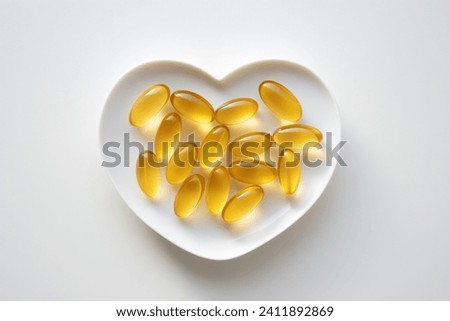 Golden shine Omega-3 capsules on heart white bowl. Medicine healthy supplement for healthy diet fish oil. White background close up top view photo.