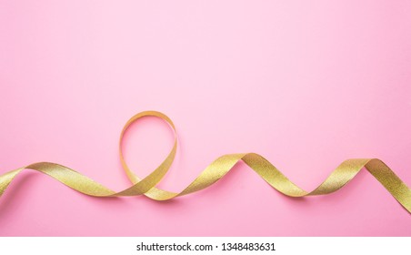 Golden Shiny Ribbon On Pink Color Background, Copy Space, Top View. Decoration, Gifts Concept