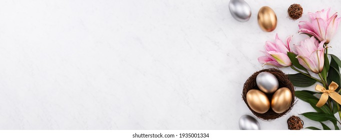 Golden And Silver Easter Eggs In The Nest With Pink Lily Flower On Bright Marble White Table Background.