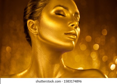 Golden skin make-up, Woman face portrait closeup. Model girl with holiday golden Glamour shiny professional make up. Gold jewellery, jewelry, accessories. Beauty gold metallic body, fashion Xmas art