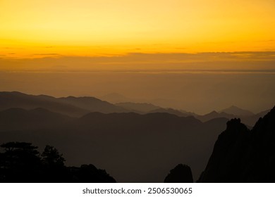 A golden sky blankets misty hills, creating silhouettes of layered mountain peaks against a serene horizon. - Powered by Shutterstock