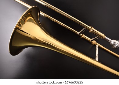 Golden slide trombone detail on black wooden table. Top view. Horizontal composition.
