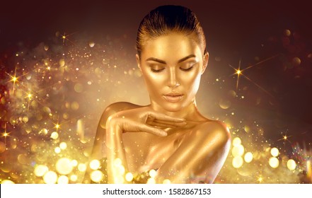 Golden sparkles skin, Woman face portrait closeup. Model girl with holiday golden Glamour shiny professional make up. Gold jewellery, jewelry, accessories. Beauty gold metallic body, fashion Xmas art.