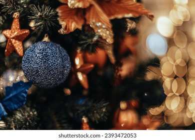 Golden star and blue Christmas ball hanging on a Christmas tree with garland lights. Decorated spruce branches.