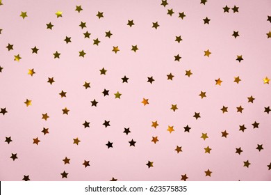 Golden star sprinkles on pink. Festive holiday background. Celebration concept. Top view, flat lay. Horizontal
