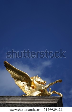 Golden statue of Pegasus horse in blue sky.