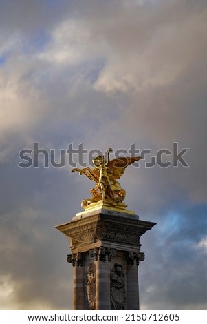 Golden statue of Pegasus horse and a woman blowing horn in cloudy sky.