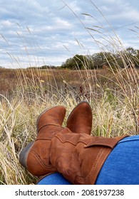 Golden Straw Natural Grass Landscape Dancing In Gentle Breeze; Blue Sky And Trees At A Distance. Brown Western Cowboy Boots And Blue Jeans. Relaxing And Grateful Point Of View - Rustic Americana Decor