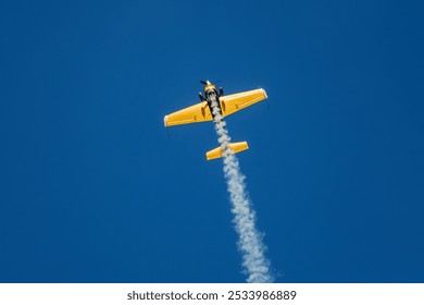 Golden stunt aerobatic plane performing stunts in blue sky with smoke trail. Concept of speed, difficulty, precision, risk - Powered by Shutterstock