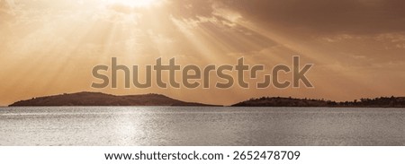 Golden sun rays streaming through fluffy clouds, illuminating a calm sea and distant islands during a breathtaking sunset