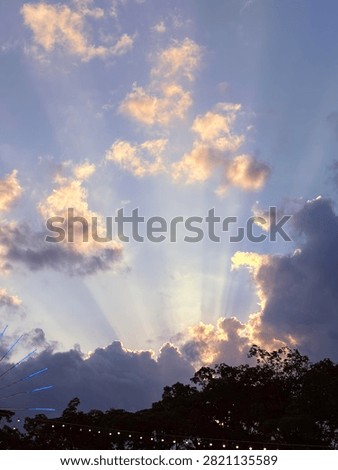 Golden sun rays streaming through dramatic clouds at sunset over treetops, creating a peaceful sky with soft blue and golden tones. Natural landscape background.