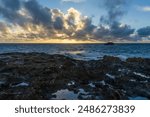 The golden sun rises over the beautiful water and rocks of Laie Point, Hawaii.