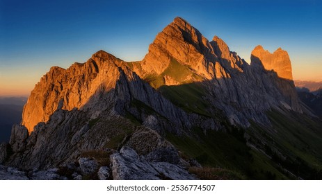 Golden sunlight illuminates a dramatic mountain range as it rises, casting long, sharp shadows over the rugged terrain, emphasizing the grandeur of the peaks. - Powered by Shutterstock