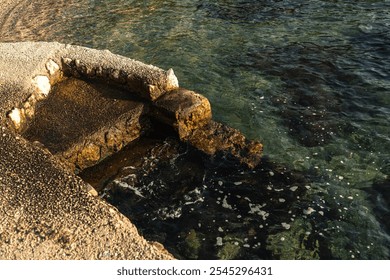 Golden sunlight illuminating the textured rocky shoreline along the clear, peaceful waters. - Powered by Shutterstock