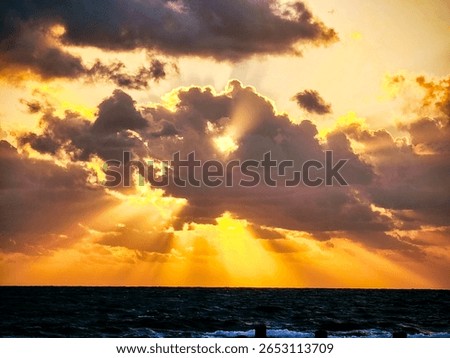 Golden sunlight streams through dramatic morning clouds over the ocean, creating a powerful and serene sunrise view.