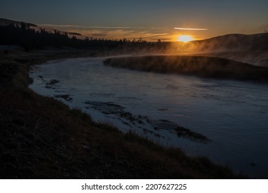 Golden Sunrise Along The Madison River In Yellowstone National Park. The Mist From The River Rises Into The Morning Rays Of Sunlight Along The Scenic Drive