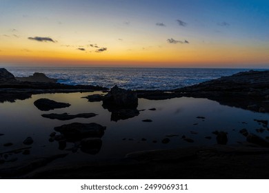 Golden sunrise reflecting on calm water in a tide pool on a rocky coastline seascape - Powered by Shutterstock