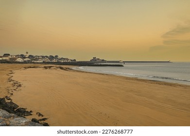 Golden sunrise of Sokoa town and port, seen from the beach promenade, on a misty winter day. In the foreground the wet sand of the beach at low tide, the calm sea, in the background the castle - Powered by Shutterstock