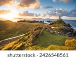 Golden sunrise at Twr Mawr Lighthouse on Ynys Llanddwyn Island on The Coast of Anglesey, North Wales with Snowdonia mountains in background.