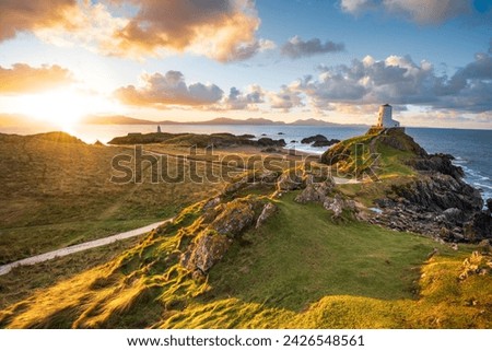 Golden sunrise at Twr Mawr Lighthouse on Ynys Llanddwyn Island on The Coast of Anglesey, North Wales with Snowdonia mountains in background.