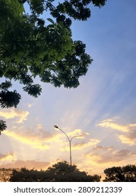 Golden sunset with dramatic sun rays shining through clouds above trees in Bandung, West Java, Indonesia.