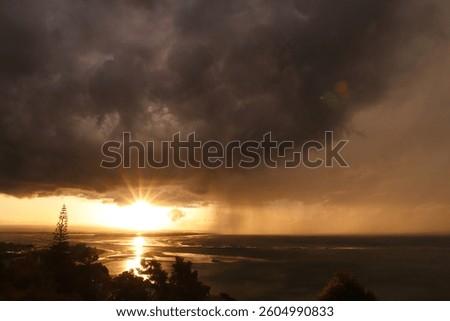 Golden sunset over the ocean with a dramatic storm in the background. Sun rays break through dark clouds, creating a stunning contrast of light and shadow. Perfect for nature and weather themes