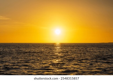 Golden sunset over the ocean with a silhouetted boat and a flying bird, reflecting warm light across the calm water. - Powered by Shutterstock