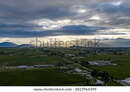 Golden sunset rays break through dramatic clouds over a green farmland valley near Chilliwack, British Columbia, Canada, creating peaceful, hopeful mood.
