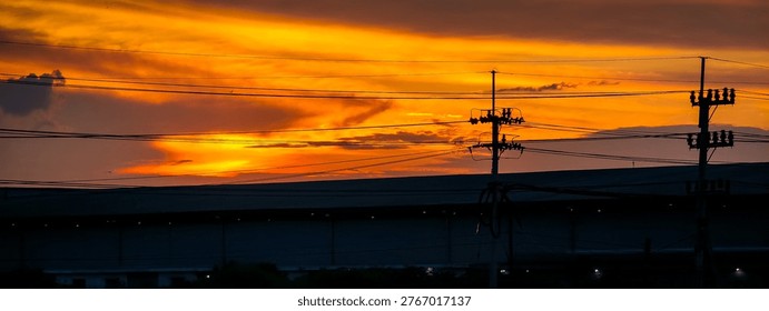 Golden sunset sky with dramatic clouds and power line silhouettes, creating a warm urban landscape atmosphere. Perfect for background, nature, and evening concept imagery.