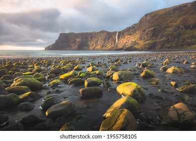 Golden sunset or sunrise light on the rocky shore seascape at low tide and Talisker Waterfall off the seaside cliff at Talisker Bay Beach on the Isle of Skye, Scotland