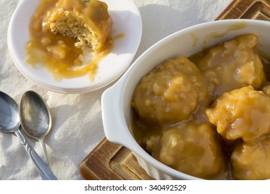 Golden Syrup Dumplings On Table With One Portion On Plate With Bite Taken From Above