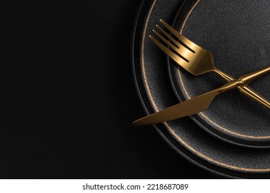 The golden tableware is placed on a ceramic dinner plate. The background is black leather. Luxurious, sumptuous fine tableware.Flat lay, top view, banner,horizontal photo - Shutterstock ID 2218687089