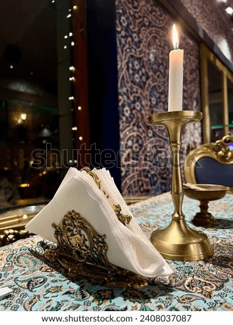 A golden tissue holder with Persian style. Standing on a restaurant table beside the golden candle holders.