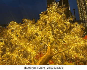 Golden tree leaves with LED twinkle lights or icicle lights. Big gold tree decorated with yellow lights to celebrate seasons greetings, holiday season of Christmas and new year. Night shot.